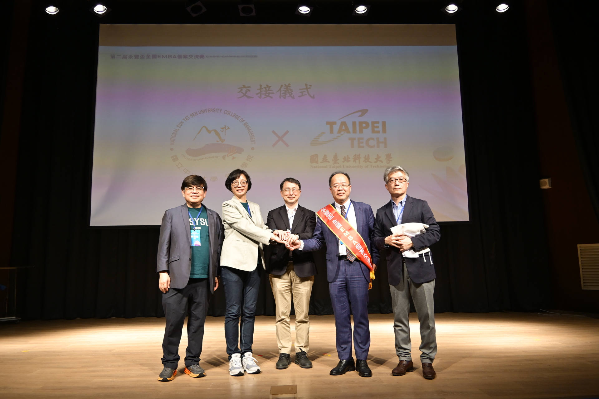 由國立中山大學EMBA執行長蔡佳芬（左二）交棒予國立臺北科技大學EMBA執行長陳育威（右二），象徵這場全國EMBA商管盛會將持續傳承、邁向下一站。圖片